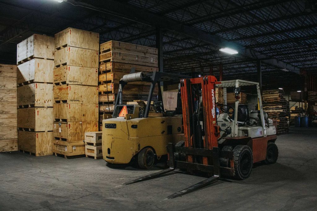 yellow and orange forklift in a warehouse with stacked wooden crates