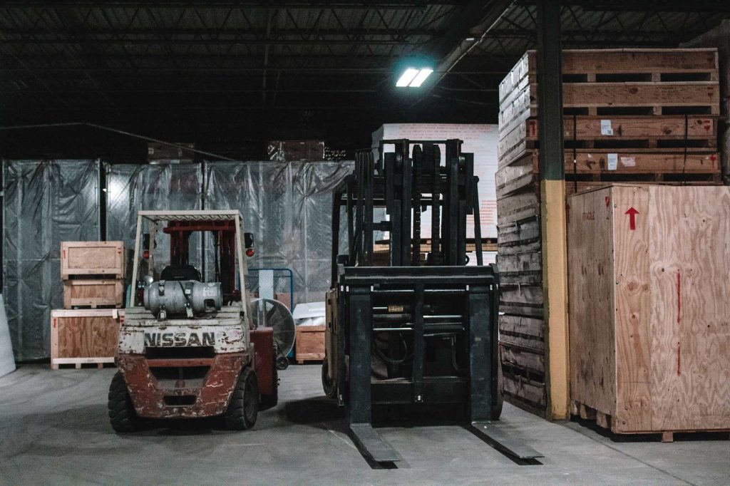 old Nissan forklift parked in a warehouse with stacked wooden crates and pallets