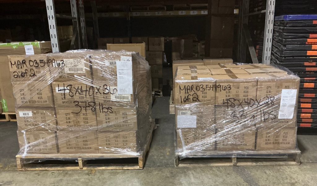 Two pallets of boxed goods secured with stretch wrap for cross-dock shipping in a warehouse.